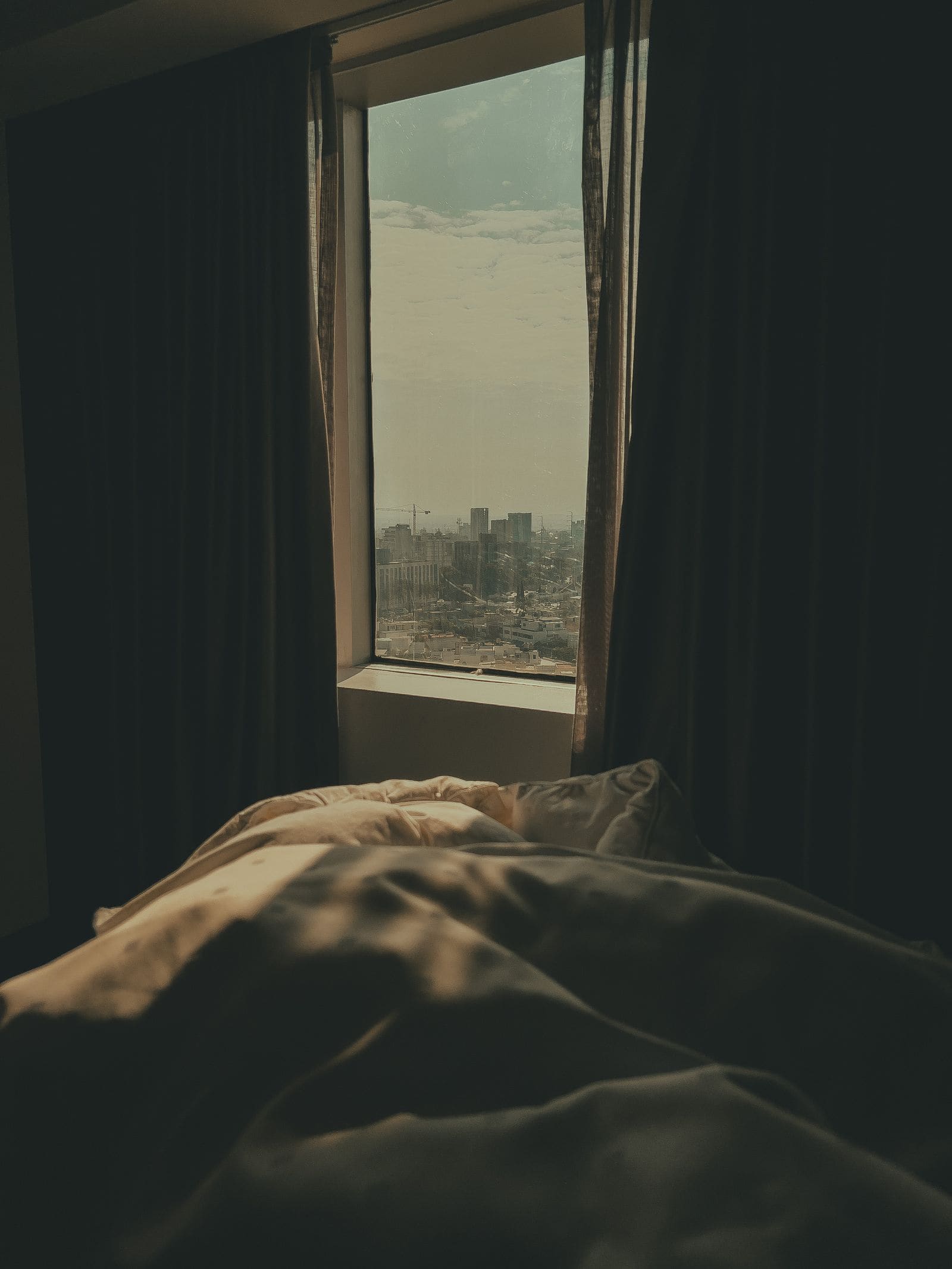 Curtained window in a dim bedroom looking out over the city skyline at night